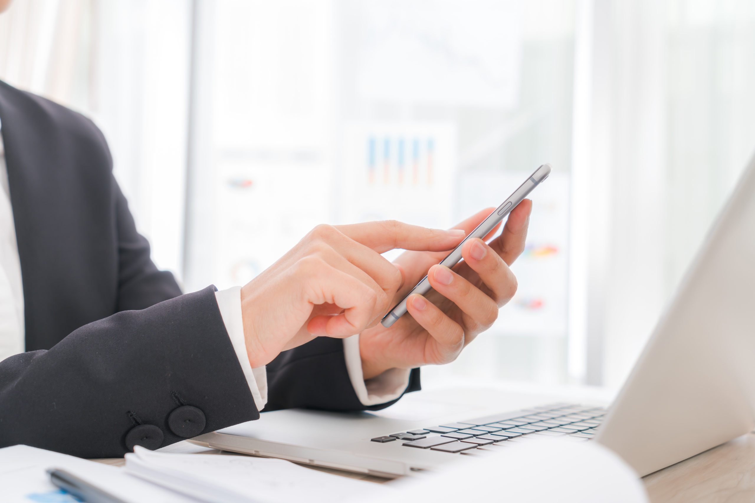 Closeup of business woman hand typing on laptop keyboard with  mobile phone